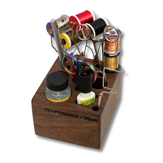 A wooden Temperance & Penn Tool Holder organizing various fly fishing tools including scissors, spools of thread, bobbin holders, and small bottles, designed for fishing tackle storage.