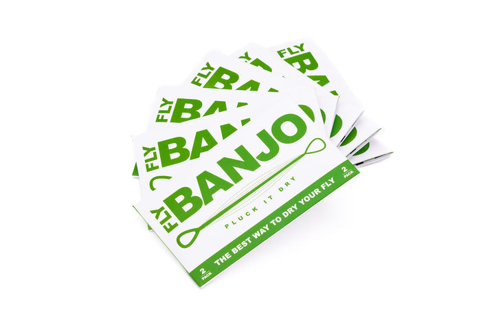 Stack of white and green packaging cards for The Fly Banjo, a fishing tackle product designed to dry flies, shown in a fanned arrangement on a white background.
