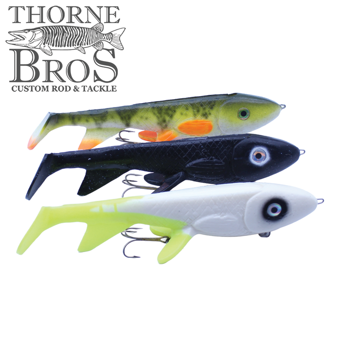 Three Trophy Systems Bait Co. 12" Stealth Bomber fishing lures in green, black, and white colors with detailed eyes and treble hooks, designed for musky fishing.