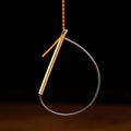TyFlyz Hackle Tweezers fishing tool with a slim brass body and a black flexible loop for securing materials, shown holding a striped orange and black fly-tying feather.