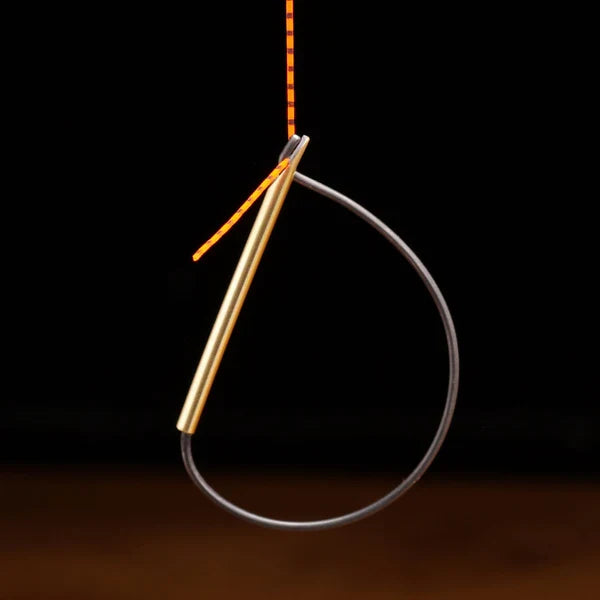 TyFlyz Hackle Tweezers fishing tool with a slim brass body and a black flexible loop for securing materials, shown holding a striped orange and black fly-tying feather.