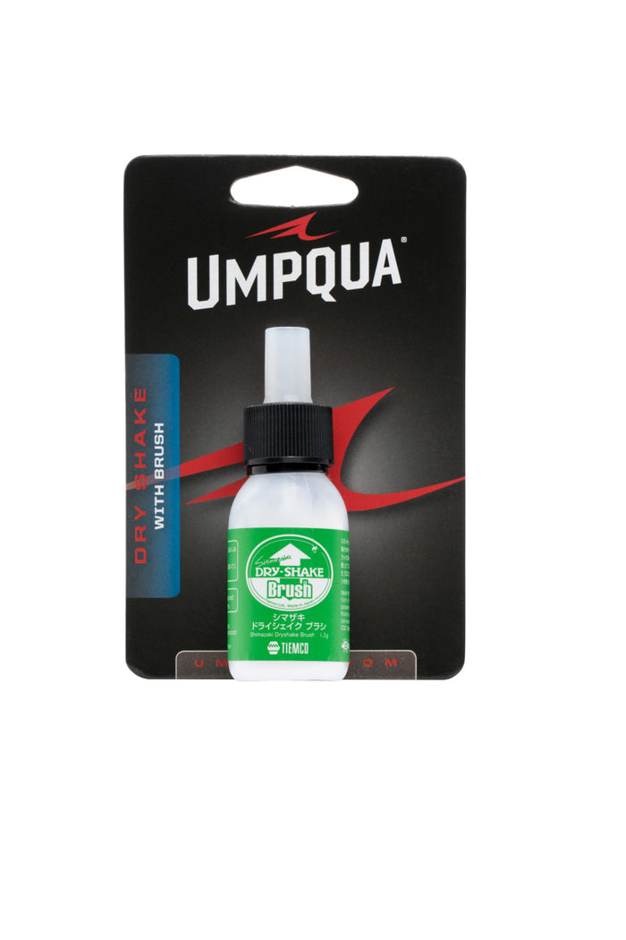 Umpqua Shimazaki Dry Shake With Brush in a small white bottle with black cap, displayed on black branded packaging with red and white text.