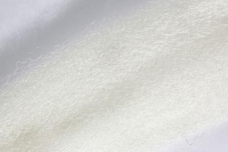 Close-up of white fibrous material with a soft, fuzzy texture used in fishing tackle, identified as Wapsi Fuzzy Fiber for fly tying and lure crafting.