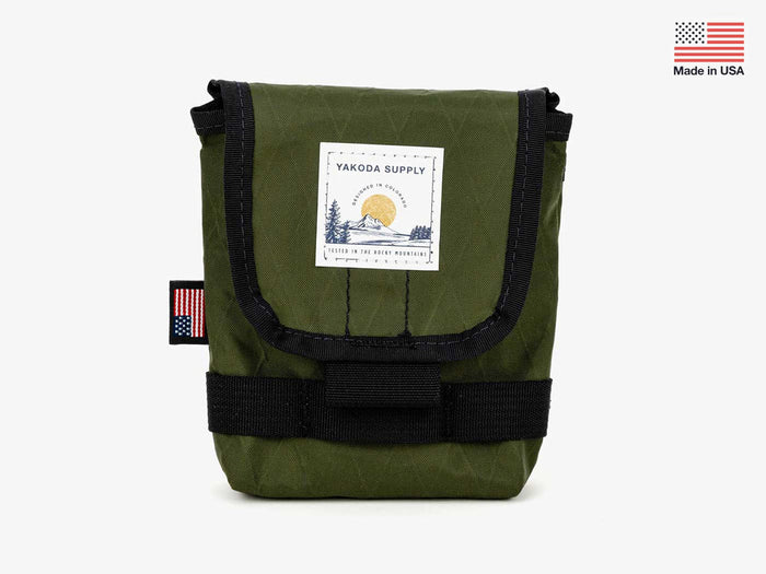 Yakoda Utility Pouch in olive green with black trim, featuring a front flap with a nature-themed logo patch, designed for storing fishing tackle and accessories.