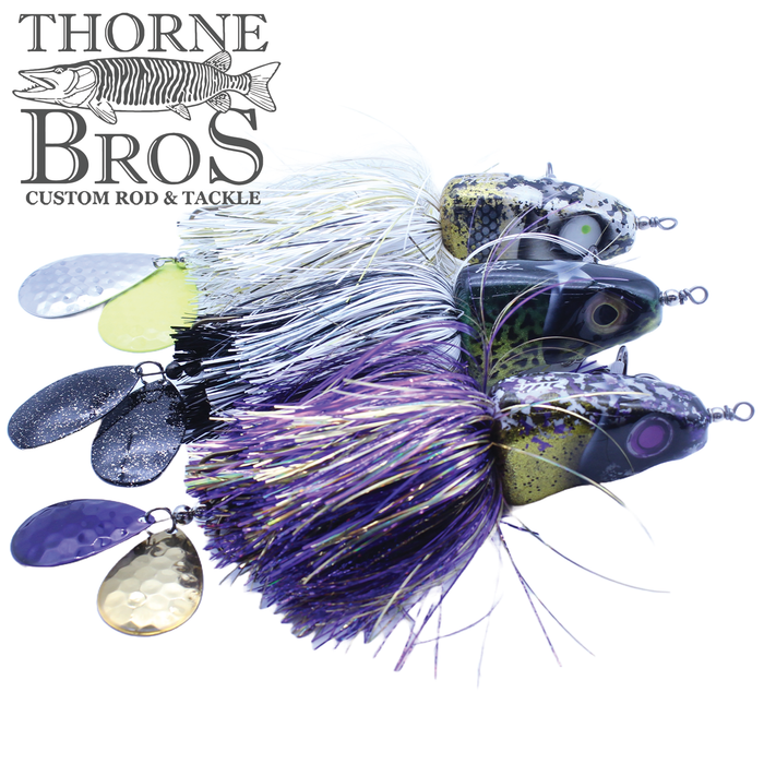 Three Zilla Baits Metal Head fishing lures with detailed heads and colorful, textured skirts in white, black, and purple, featuring metallic spinner blades attached to each lure.
